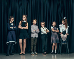 Cute surprised stylish children on dark background. Beautiful stylish teen girls and boy standing together and posing on the school stage in front of the curtain. Classic style. Kids fashion and