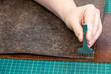 craftsman punches edge of leather item for handbag