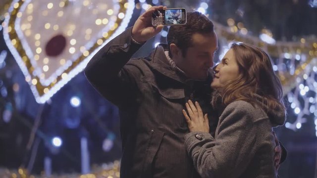 Couple of romantic couple taking selfie at Christmas tree outdoor, kiss