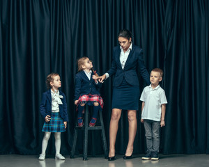 Cute smiling happy stylish children and female teacher on dark background. Beautiful stylish teen girls and boy standing together and posing on the school stage in front of the curtain. Classic style