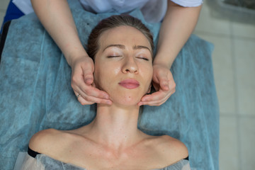 Top view of the face of a young girl during manual massage of the face in the spa. Shiatsu massage. Anti-aging facial massage for a beautiful blonde woman.
