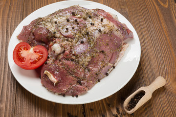 pickled turkey meat with spices on a white plate, next to a sliced tomato, surrounded by scattered peppers, on wooden boards