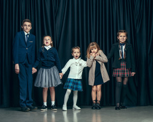 Cute surprised stylish children on dark background. Beautiful stylish teen girls and boy standing together and posing on the school stage in front of the curtain. Classic style. Kids fashion and