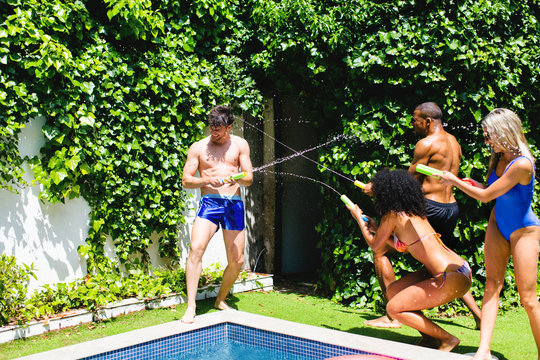 Multiethnic group of friends having fun doing water battle with toy guns.