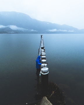 A young person walks along a wooden structure above the water on a rainy and foggy day in Squamish BC