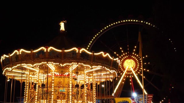 Flashing lights night illumination at amusement park carnival on vintage merry go round ferris wheel funfair attraction