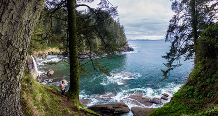 A panoramic view of a deep blue inlet with a waterfall plunging into it on the west coast of BC