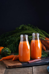 Carrot juice and carrot with leaves on black and wooden background