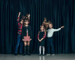 Cute surprised stylish children on dark background. Beautiful stylish teen girls and boy standing together and posing on the school stage in front of the curtain. Classic style. Kids fashion and