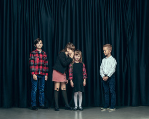 Cute surprised stylish children on dark background. Beautiful stylish teen girls and boy standing together and posing on the school stage in front of the curtain. Classic style. Kids fashion and