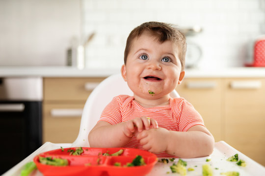Smiling chubby baby eating broccoli