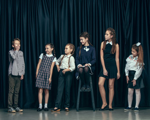 Cute surprised stylish children on dark background. Beautiful stylish teen girls and boy standing together and posing on the school stage in front of the curtain. Classic style. Kids fashion and