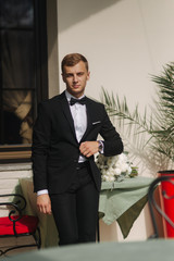 Attractive groom in wedding suit stand by the hotel. The groom wears a bow tie