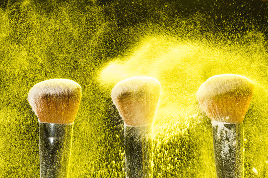 Mineral make up and objects concept - Three make up brushers in yellow dust over dark background