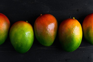 Fototapeta na wymiar Several fresh ripe mexican mangoes lie on a dark background. Whole mango, composition in a dark manner.