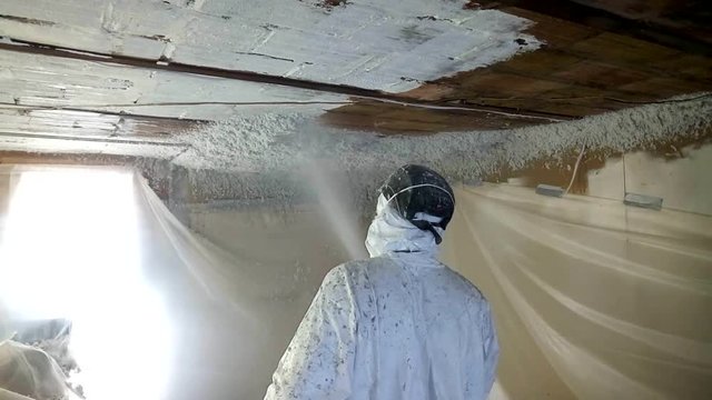 Workman spraying foam insulation material into ceiling in old cave.
