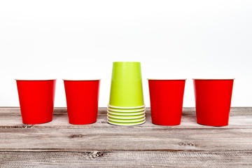 Four red and stack of green paper disposable cups for coffee and nonalcoholic drinks on wooden background