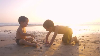 4K Slow motion - Two little brothersplaying and enjoying with teh sand in the beach at sunset