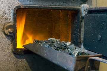 Hot water boiler with open door and fire inside and scoop with coal