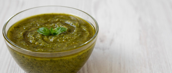 Bowl of freshly made basil pesto on white wooden background, side view. Closeup. Copy space.