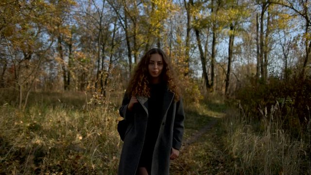Young woman slowly walking in autumn park, shallow depth of field, slow motion