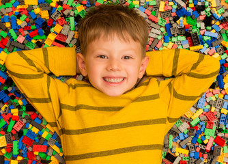 Happy little boy with smiley face resting between colored plastic building blocks