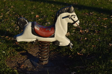 Old playground white rocking horse on large spring in a park