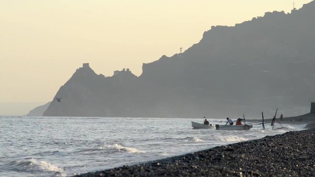 Pescatori mettono in acqua le loro barche per la pesca notturna,mentre gabbiani volteggiano ed il sole &egrave; tramontato in una giornata ventosa    