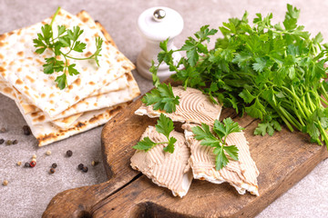 Pieces of matzah with homemade liver pate with parsley and onion on old wooden cutting board with burlap napkin. Gray marble background. Copy space