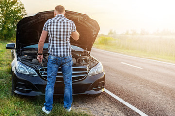 man with a wrench in front of the open hood of a broken car - obrazy, fototapety, plakaty
