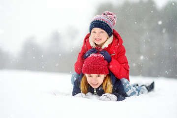 Two adorable little girls having fun together in beautiful winter park. Beautiful sisters playing in a snow.