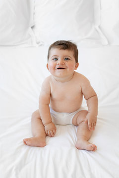 Happy chubby baby siting on white bed