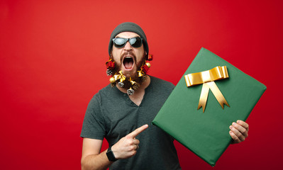 Amazed bearded man pointing at big gift box for christmas or new  year over red background
