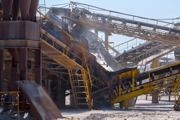 Naklejka premium Crushing machinery, cone type rock crusher, conveying crushed granite gravel stone in a quarry open pit mining. Processing plant for crushed stone and gravel. Mining and Quarry mining equipment.