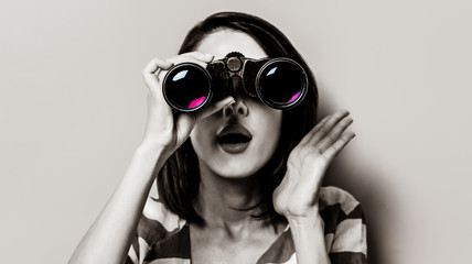 portrait of the beautiful young woman with binoculars on the yellow background. Image in black and...
