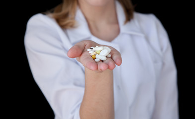 Front view of a young intellectual doctor on a black background with text space. The medical worker provider offers a pill