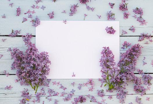 Fototapeta Lilac spring flowers with blank paper for greeting message on a light blue shabby wooden background. Vintage Floral mock up with purple flowers. Copy space