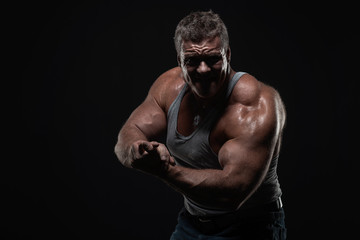 Obraz na płótnie Canvas powerful muscular man shows biceps on a black background. Strength and fitness concept