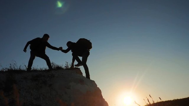 silhouette two men teamwork tourists climber climbs a mountain. walking tourist hiking adventure climbers sunset climb the mountain . slow motion video. hiker sunlight on top win victory the hill