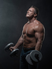 Fototapeta na wymiar muscular man trains with dumbbells on black background in smoke