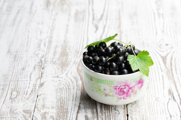 Fresh black currant in ceramic bowl on white wooden table