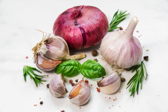 garlic with red onion, basil, rosemary and peppercorn on white marble background. close up