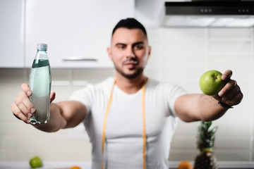 bottle of water and an apple close-up in the hands of an athletic man in the kitchen
