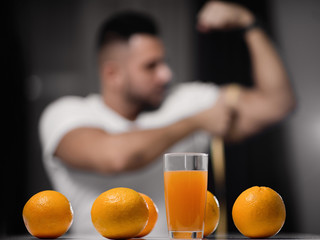 glass of juice and oranges close-up on the background of a man who measures his bicep with a measuring tape