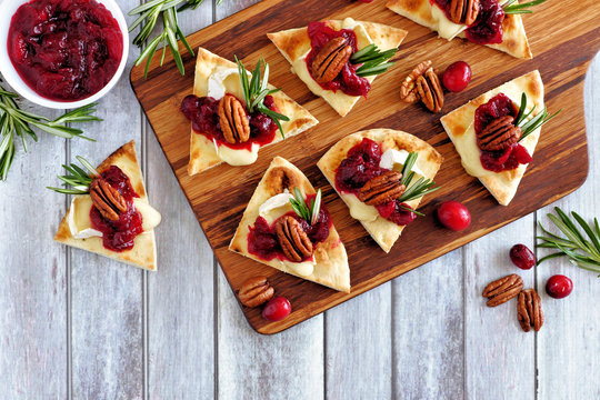 Fototapeta Holiday flatbread appetizers with cranberries, pecans and brie cheese. Top view table scene on a wooden platter.
