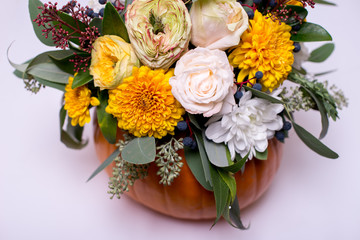 Autumn floral bouquet in a pumpkin vase on a light background, a mixture of flowers, pionic rose, eucalyptus, chrysanthemum