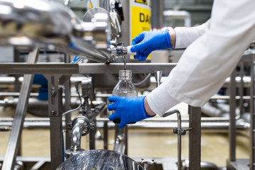 Worker at bottling factory checking juice quality.