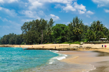Beautiful seascape with sea and rock in Nang Thong Beach, Khao Lak, Thailand. View of bright blue sea with protruding stones in the foreground and crowded beach with bathing and walking people