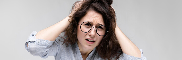 Obraz premium Young brunette girl with glasses. The girl grabbed her head and shouted.