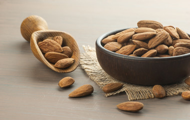 Almonds nuts in dark Brown bowl on rustic vintage painted wooden table with wooden spoon or scoop close up. Almond background concept with copy space
